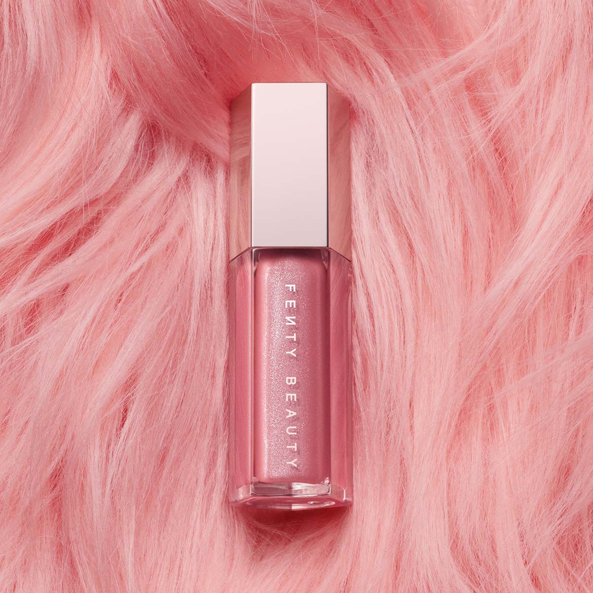 Roze Fenty Beauty lipgloss met zilveren dop, liggend op een zachte, roze achtergrond.