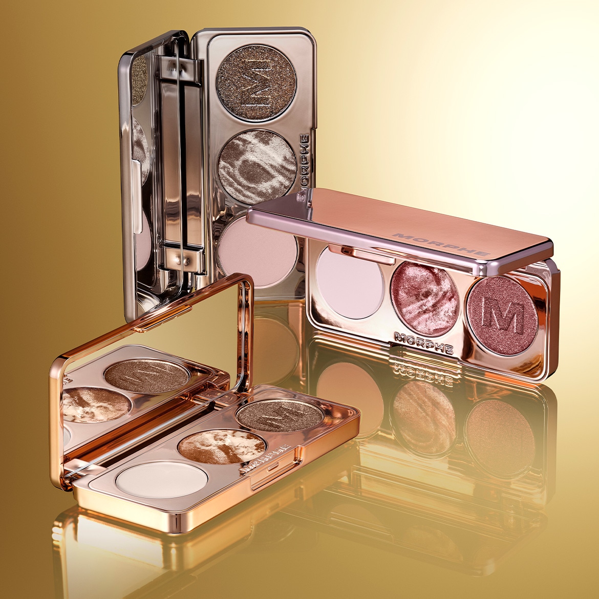 Drie Morphe oogschaduwpaletten in roségouden verpakking met verschillende kleuren oogschaduw, van glanzend bruin tot zachtroze, klaar om je ogen te laten stralen.