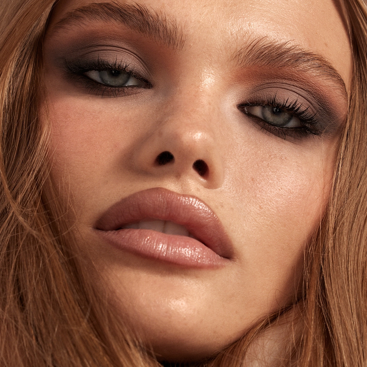 Een close-up van een vrouw met een glamoureuze make-up look, met donkere oogschaduw en glanzende lippen, die haar gezicht en haar benadrukt.