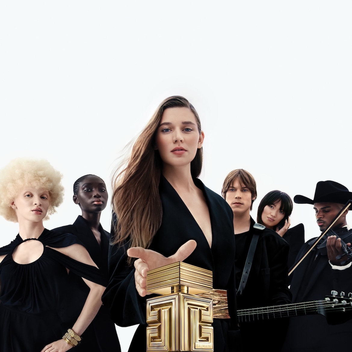 Een diverse groep mensen, waaronder een vrouw met lang bruin haar die een gouden Balmain-parfumflesje vasthoudt, staat voor een witte achtergrond.
