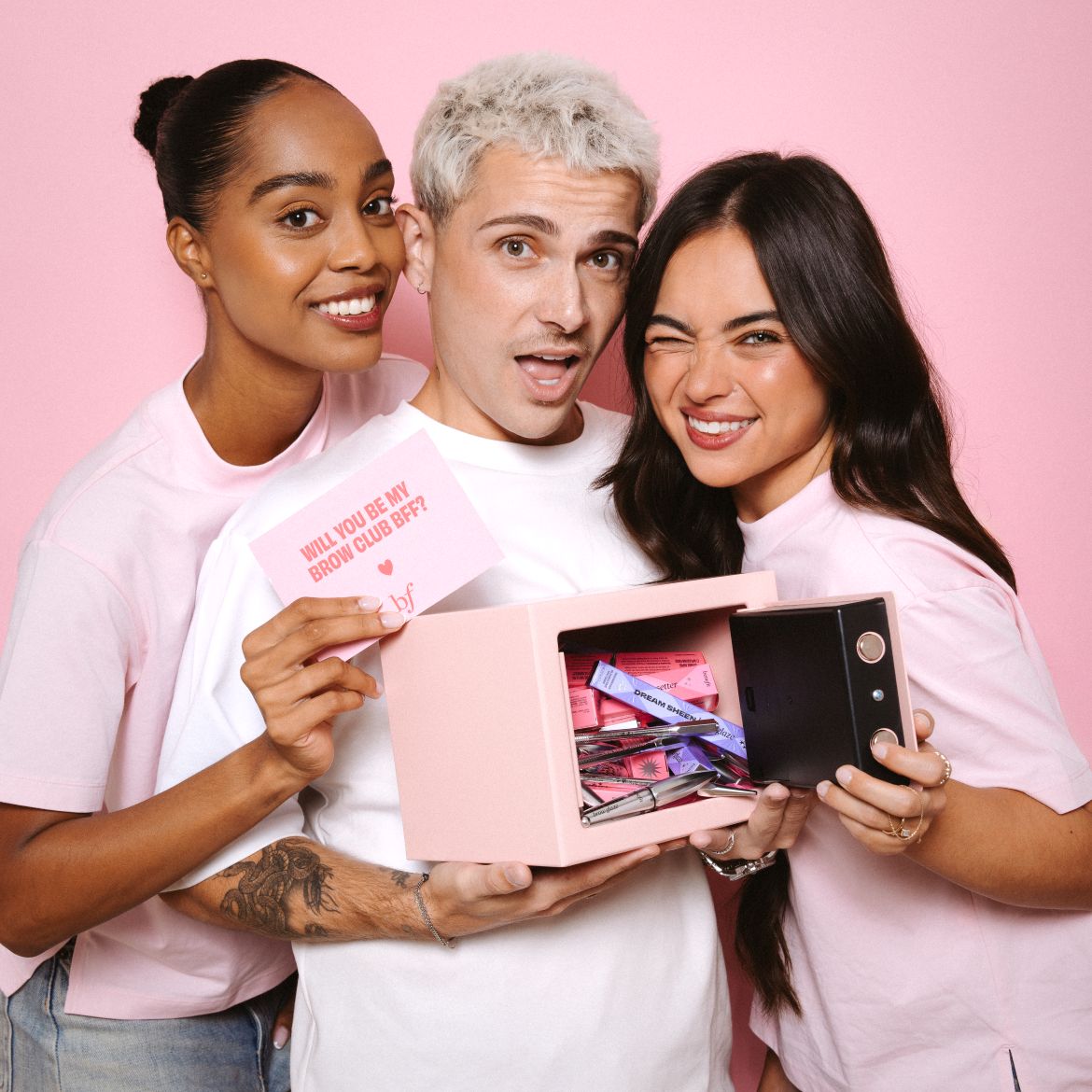 Drie modellen poseren met een roze kluisje vol Benefit-wenkbrauwproducten en een kaartje met de tekst "WILL YOU BE MY BROW CLUB BFF?".