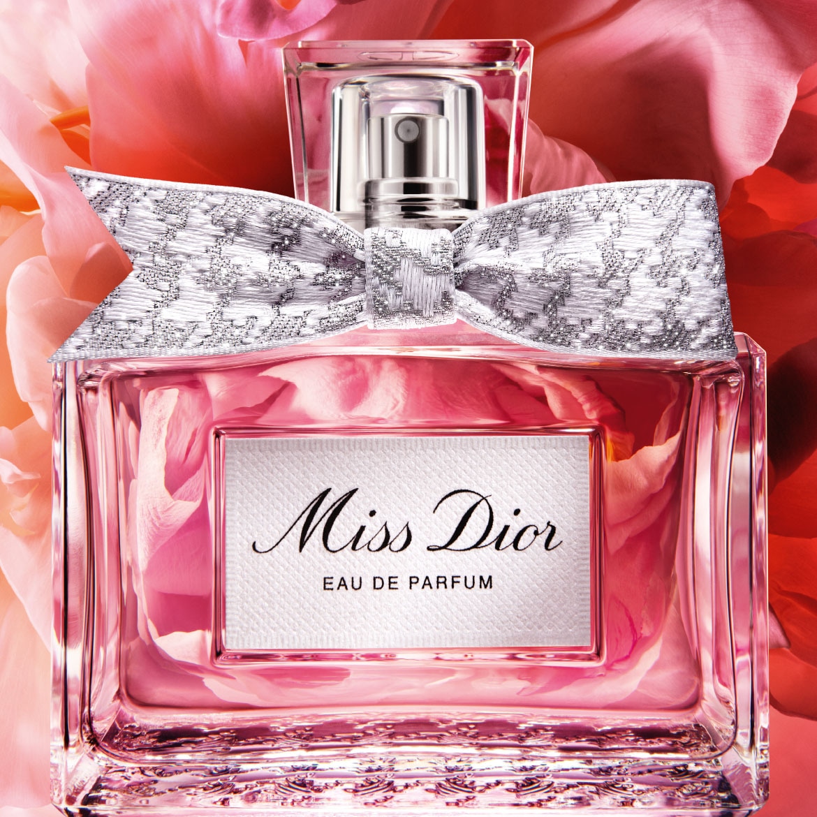 De Miss Dior Eau de Parfum is een roze vloeistof in een glazen fles met een zilveren strik en de tekst "Miss Dior EAU DE PARFUM" op een wit etiket, omringd door roze bloemblaadjes.