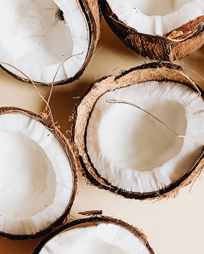 Een close-up van verschillende opengebroken kokosnoten, waarbij het witte vruchtvlees en de bruine schil duidelijk te zien zijn.