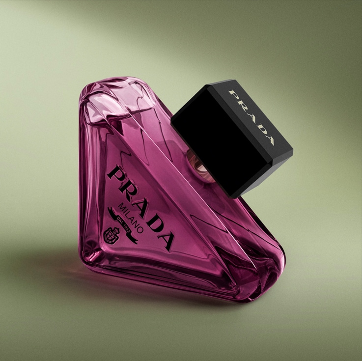 De Prada Paradoxe Intense Eau de Parfum is een roze parfumflesje met een zwarte dop, liggend op een lichtgroene achtergrond.