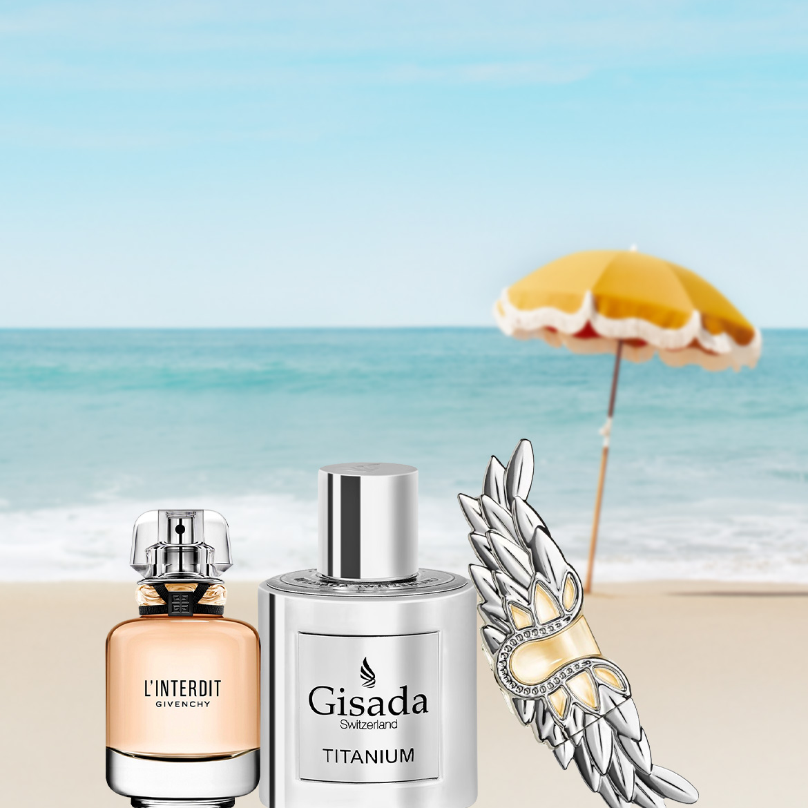 Twee parfumflesjes, L'Interdit Givenchy en Gisada Titanium, staan op een zandstrand met de oceaan en een gele parasol op de achtergrond, naast een zilveren vleugelvormige broche met gouden accenten.