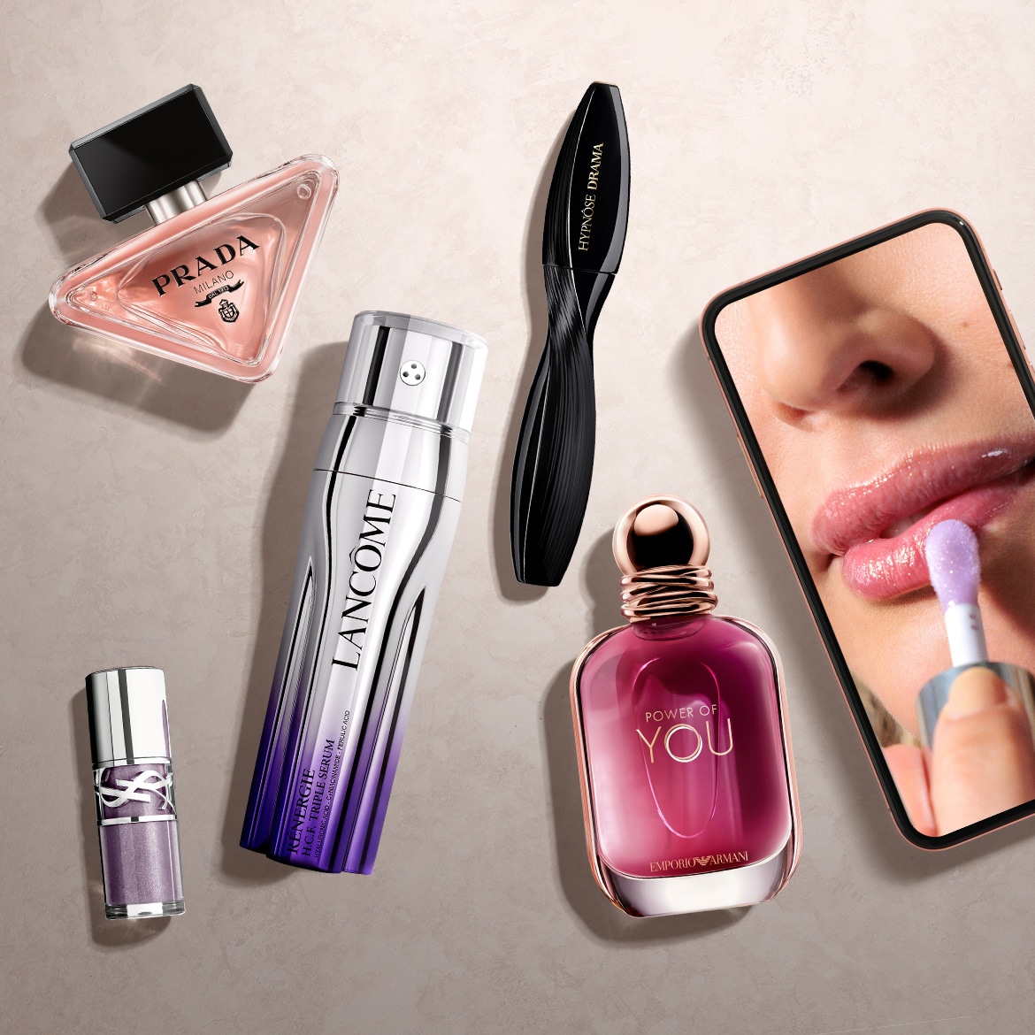 Een collectie van luxe beautyproducten, waaronder een driehoekige Prada Milano parfumfles, een Lancôme Rénergie H.C.F. Triple Serum, een Hypnôse Drama mascara, een Emporio Armani Power of You parfum en een YSL lipgloss.