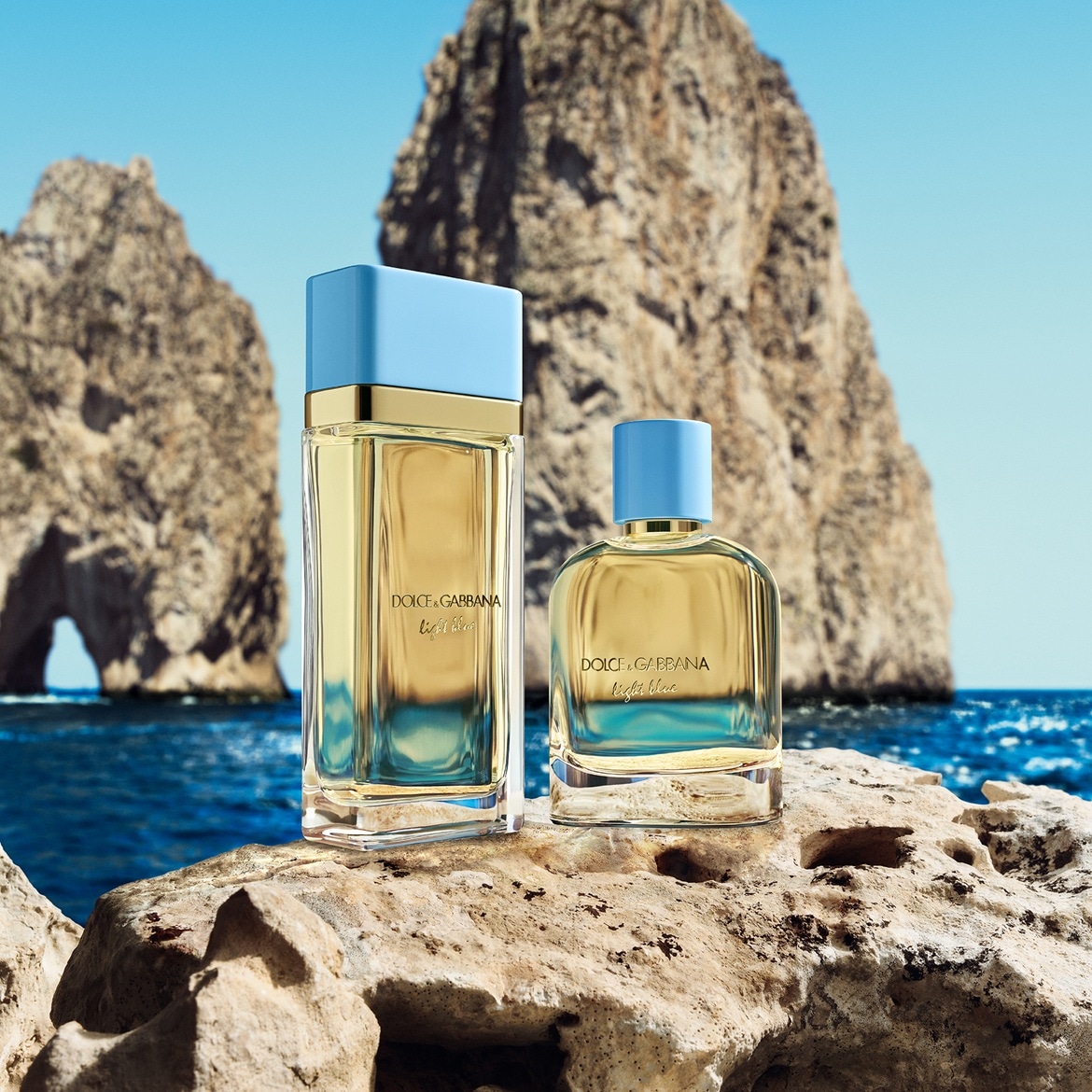 Twee flessen Dolce & Gabbana Light Blue parfum staan op een rotsachtige ondergrond, met de zee en rotsformaties op de achtergrond.