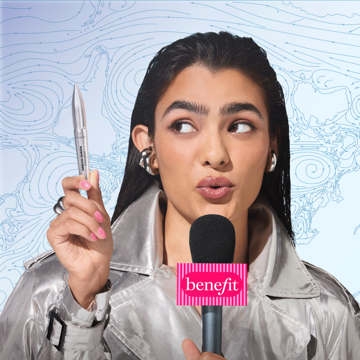 Een vrouw in een zilveren jas houdt een Benefit Dream Sheen Brow Glaze vast, klaar om je wenkbrauwen te laten stralen.