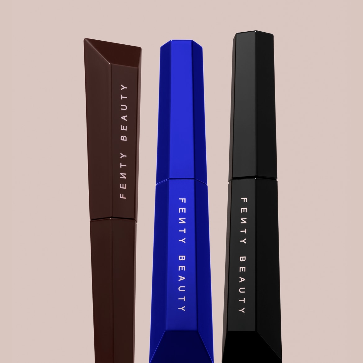 Drie Fenty Beauty mascara's in bruine, blauwe en zwarte verpakkingen staan rechtop, met het merklogo verticaal op elke tube.
