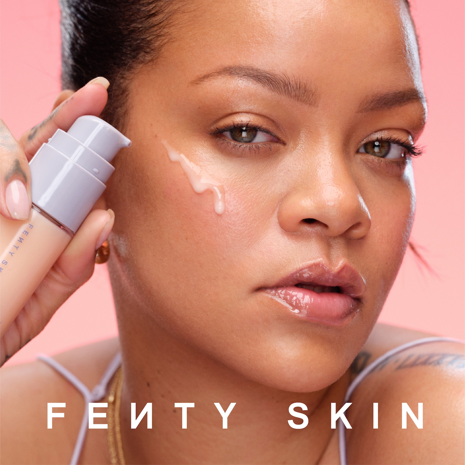 Rihanna demonstreert Fenty Skin met een druppel serum op haar gezicht, gepresenteerd in een zachtroze verpakking.