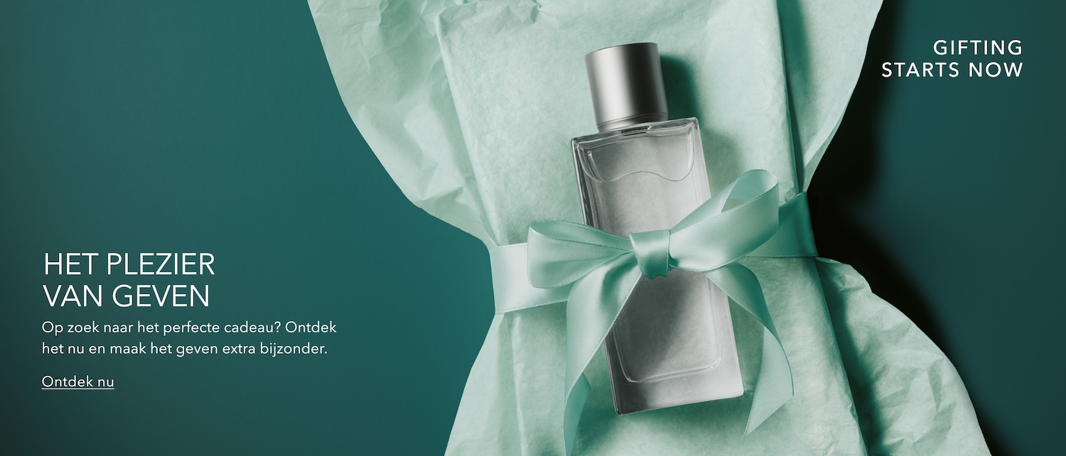 Een elegant parfumflesje met een zilverkleurige dop, verpakt in lichtgroen vloeipapier en vastgebonden met een bijpassend lint, met de tekst "GIFTING STARTS NOW" en "HET PLEZIER VAN GEVEN".