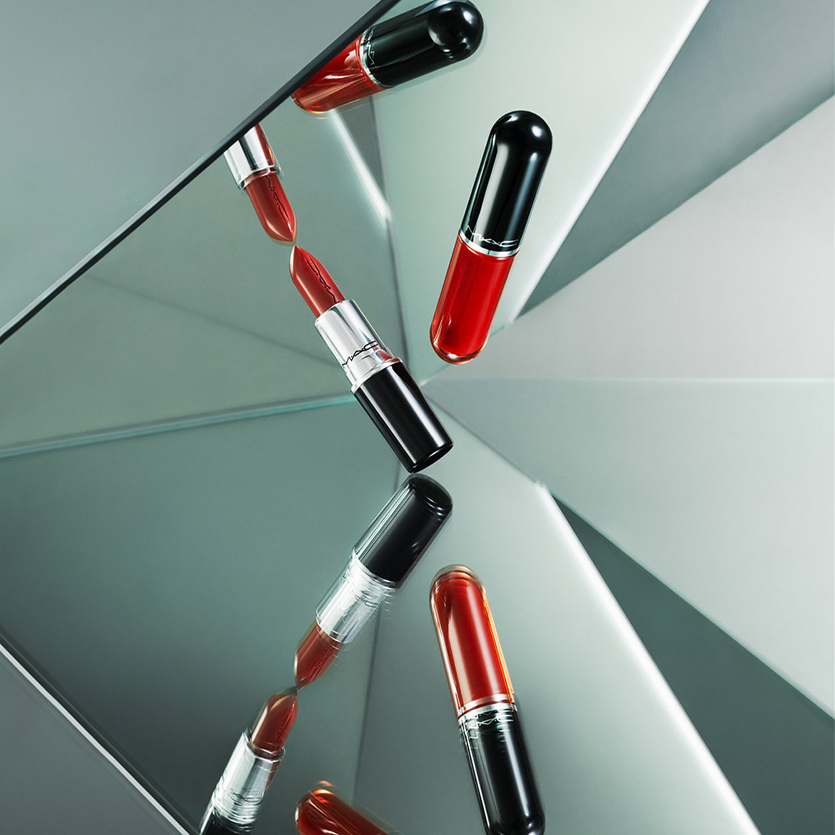 Drie MAC Cosmetics lippenstiften en lipgloss in verschillende tinten rood en oranje, gereflecteerd op een spiegelend oppervlak, creëren een dynamisch en artistiek beeld.