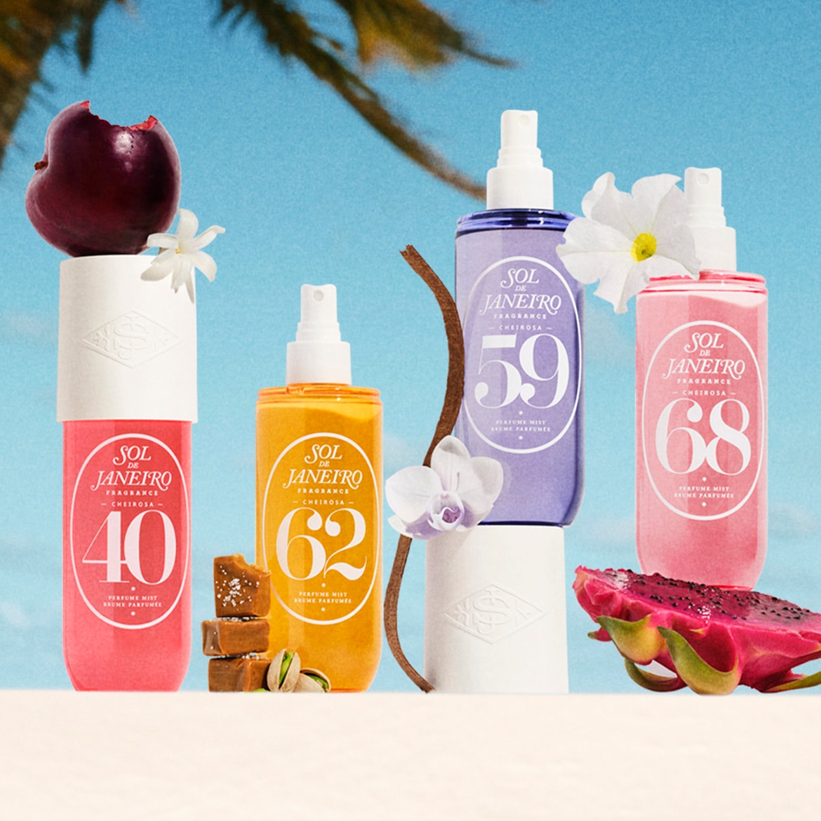 Vier Sol de Janeiro Cheirosa parfumverstuivers in roze, geel, paars en lichtroze, elk met een nummer (40, 62, 59, 68) en omringd door fruit en bloemen, staan op een zandkleurige ondergrond met een blauwe lucht op de achtergrond.