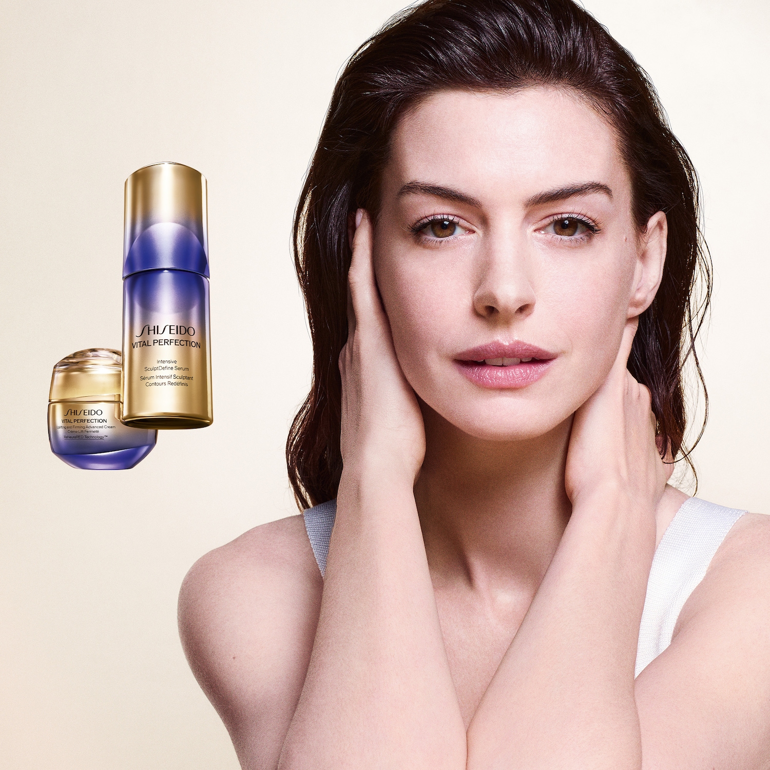 Een vrouw met donkerbruin haar en een lichte huidskleur houdt haar handen tegen haar gezicht, met op de achtergrond twee Shiseido Vital Perfection producten: een crème in een goudkleurige pot en een serum in een paarse fles.
