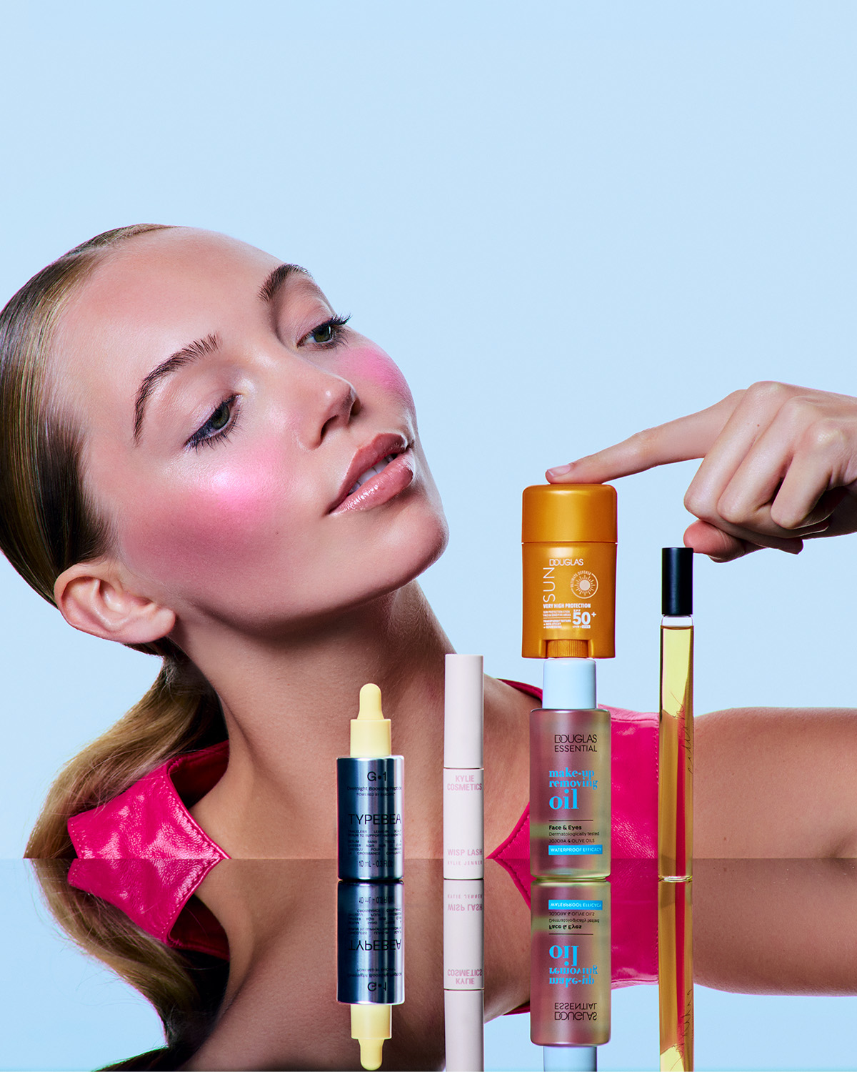 Ontdek een reeks schoonheidsproducten, waaronder TYPEBEA G-1, Kylie Cosmetics Wisp Lash en Douglas Essential make-upreinigingsolie, gepresenteerd op een reflecterend oppervlak.